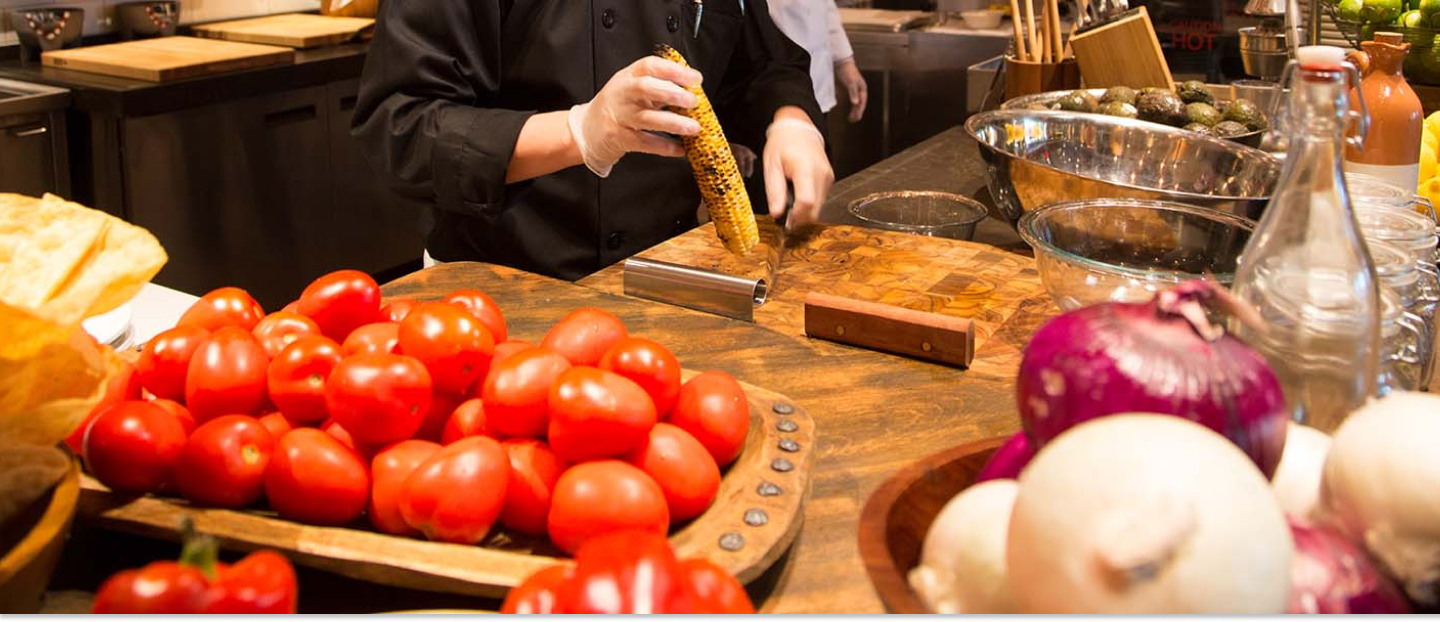 chef cutting corn on a cutting board with tomatoes