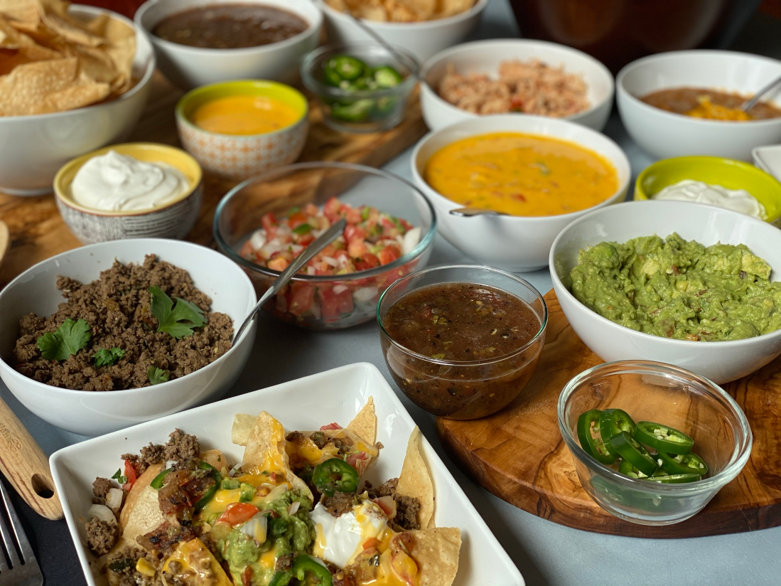 a layout of food that includes nachos, ground beef, guacamole, salsa and jaepenos