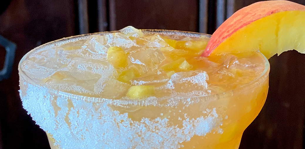 Uncle Julio's August margarita of the Month, peach, with a peach slice and sugar on the rim of the glass.