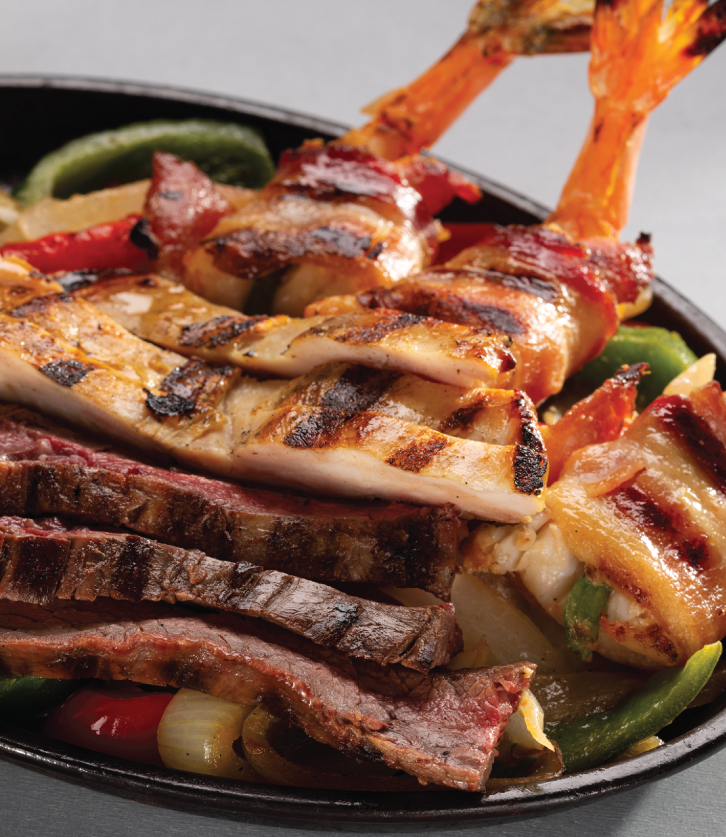 Chicken and steak fajitas on top of a bed of grilled onions and bell peppers